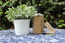 Load image into Gallery viewer, 16oz hand lotion on a table next to a plant on one side and a fragrance stick on the other